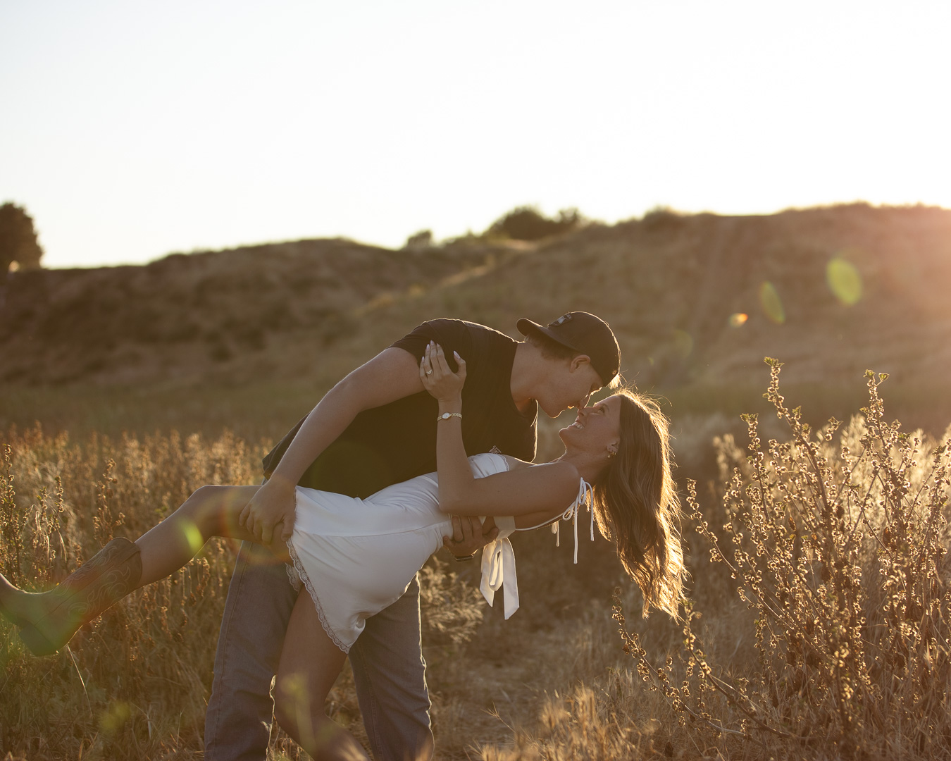 Man dipping his partner in a playful kiss in a golden sunlit field